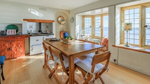 Een keuken met een houten tafel en stoelen, een fornuis en een spoelbak. Er zijn ramen met uitzicht op de zee.
