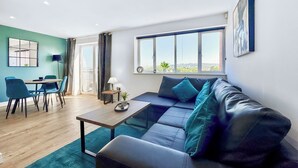 Ein modernes Wohnzimmer mit einer Couch, einem Esstisch und Stühlen. Ein Fenster bietet Blick auf die Stadt.