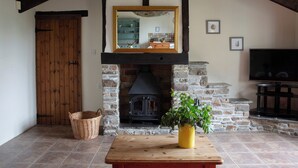 Un salón acogedor con chimenea de piedra, vigas de madera, un televisor y una mesa con un jarrón.