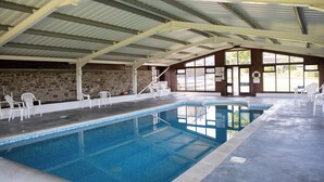 Una piscina interior con agua cristalina, rodeada de sillas blancas y una pared de piedra.