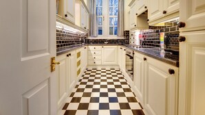 Een keuken met geruit vloerkleed, witte keukenkastjes en een raam met gordijnen.