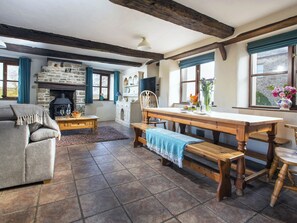 A cozy living room with a stone fireplace, wooden furniture, and a view of the garden through the windows. - Jasmine Cottage - UKC4694 (Woodford, near Bude)