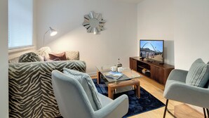 Ett modernt vardagsrum med en soffa, fåtöljer, ett soffbord, en tv och en dekorativ spegel.
