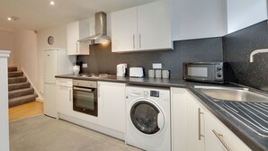 Ett modernt kök med vita skåp, en rostfri köksfläkt, en inbyggd ugn, en mikrovågsugn, en tvättmaskin och ett diskho.
