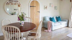 A dining area with a wooden table and chairs, a mirror, and a floral vase. - The Stables - UKC4696 (Woodford, near Bude)
