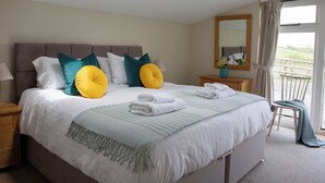 A bedroom with a large bed, a skylight, a balcony with a chair, and a view of the outdoors. - The Stables - UKC4696 (Woodford, near Bude)