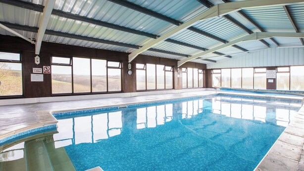 Une piscine intérieure à l’eau d’un bleu limpide, dotée de grandes fenêtres et d’un plafond haut.