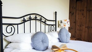 Un lit bien fait, avec du linge de lit blanc, des oreillers gris et un plateau en bois sur lequel se trouvent un livre et des verres de jus d’orange.