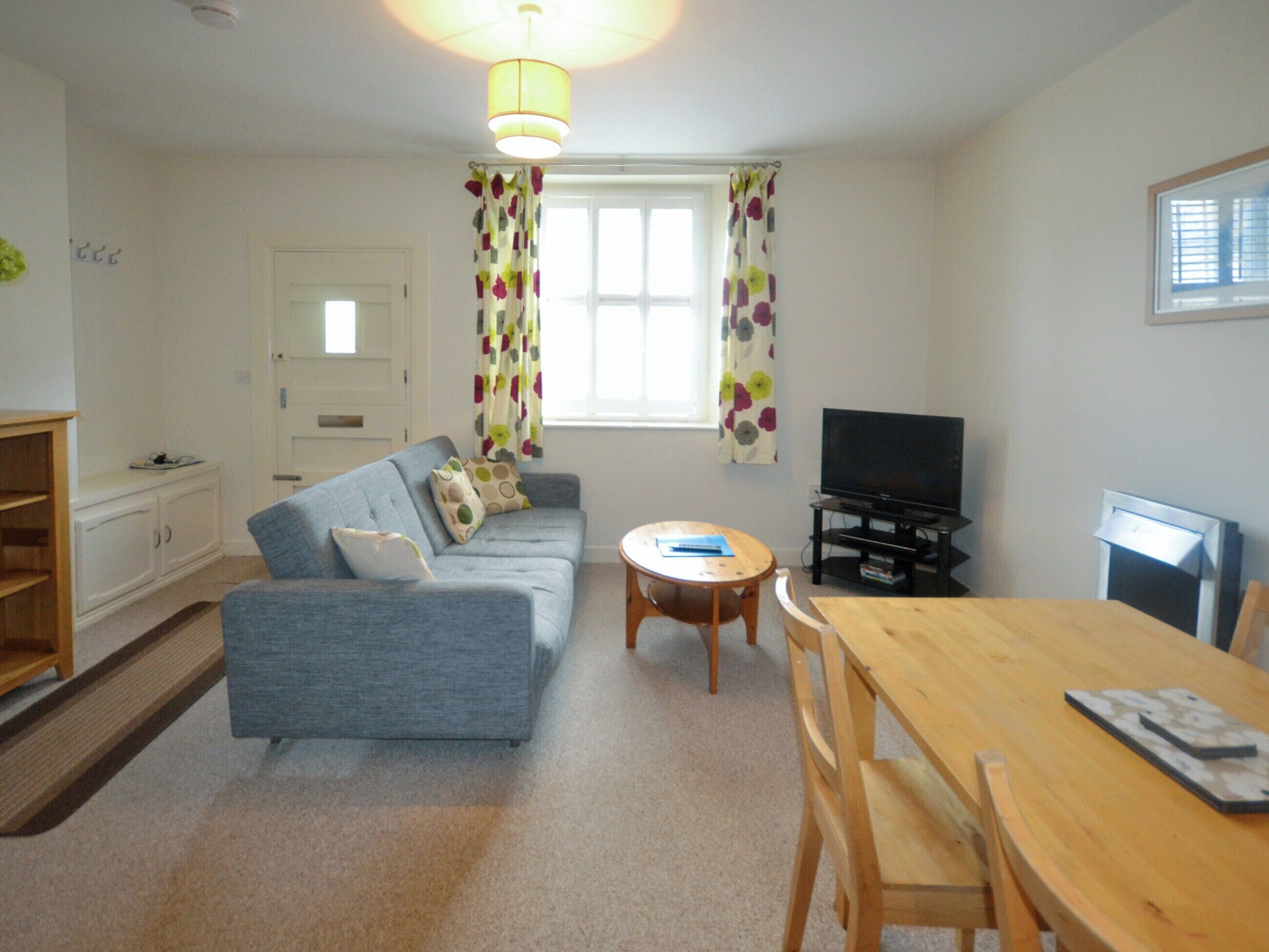 A living room with a sofa, a TV, a wooden table, and a window with curtains.
