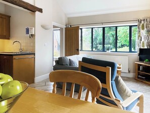 A cozy kitchen with a dining area, a window with a view of greenery, and a television on a wooden stand.