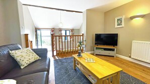 Een woonkamer met een bank, salontafel, televisie en een trap naar een hoger gelegen verdieping.