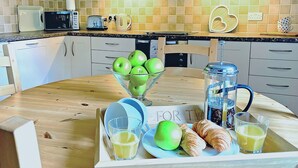 Een keuken met een houten tafel gedekt voor het ontbijt, inclusief appels, croissants en sapglazen.