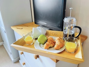 Un safata d'esmorzar amb croissants, una poma verda, suc d'aranja i una cafetera.