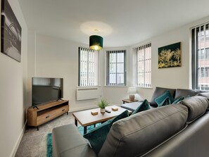 A modern living room with a sofa, TV, and a small table with a lamp. - 1 bedroom accommodation in Newcastle Upon Tyne (Newcastle Upon Tyne)