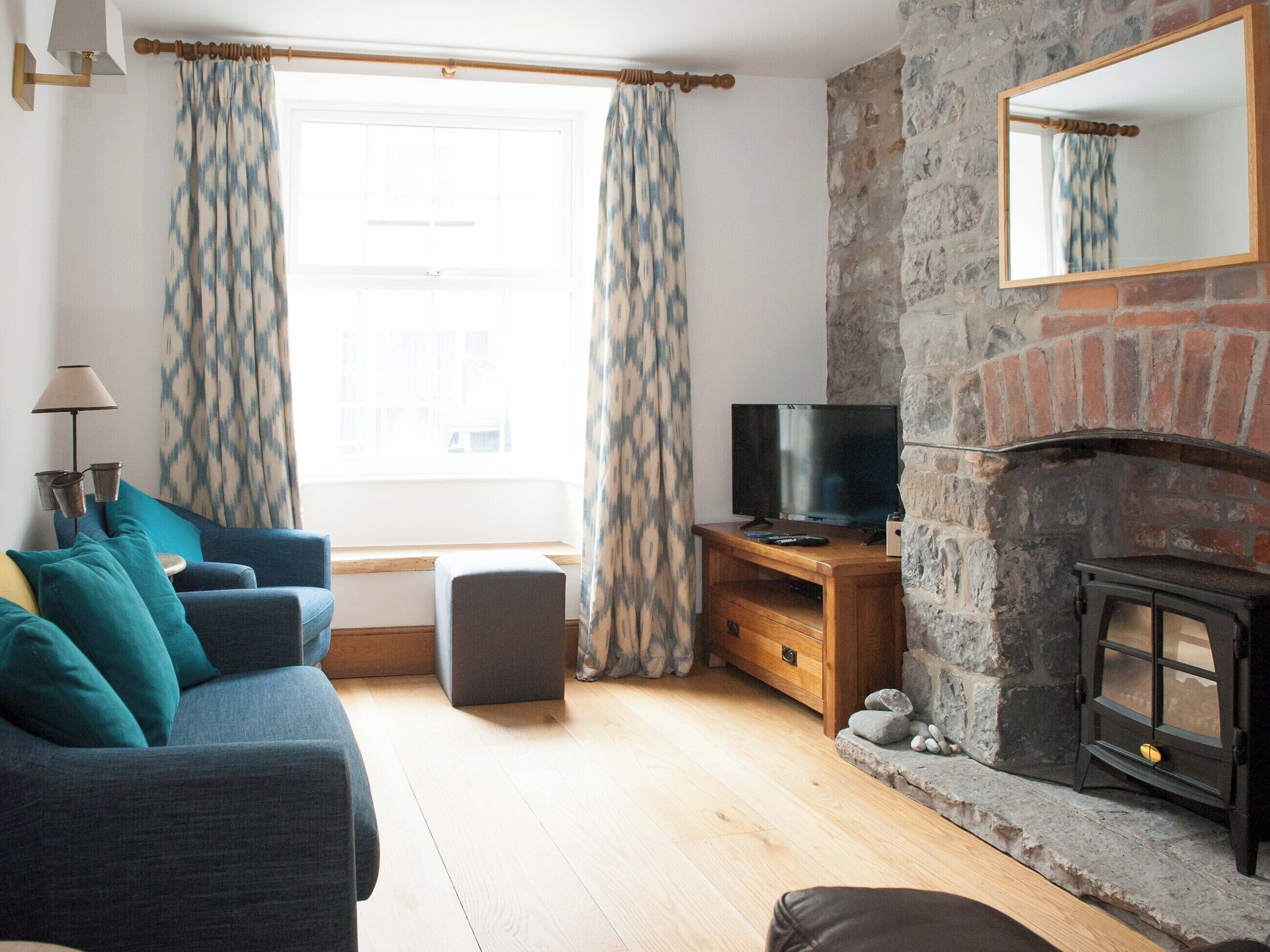 A living room with a sofa, a television, a fireplace, and a window with patterned curtains.