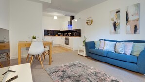 Ein modernes Wohnzimmer mit einem blauen Sofa, einem Essbereich mit Holztisch und einer Küche im Hintergrund.