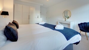 Ein modernes Hotelzimmer mit einem großen Bett, einem weißen Kleiderschrank und einem Schreibtisch mit Spiegel.