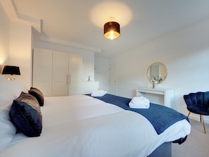 Ein modernes Hotelzimmer mit einem großen Bett, einem weißen Kleiderschrank und einem Schreibtisch mit Spiegel.