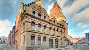 Ein historisches Gebäude mit einem markanten Turm, großen Fenstern und einer Steinfassade.