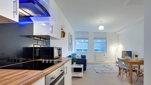 Eine moderne Küche mit Einbauofen, Mikrowelle und Herd. Es gibt einen Essbereich mit Tisch und Stühlen sowie ein Wohnzimmer mit Sofa und Couchtisch.