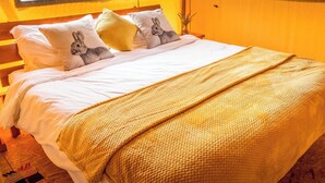Ein Bett mit weißer Bettwäsche, einer gelben Strickdecke und Kissen mit Hasenmotiven.