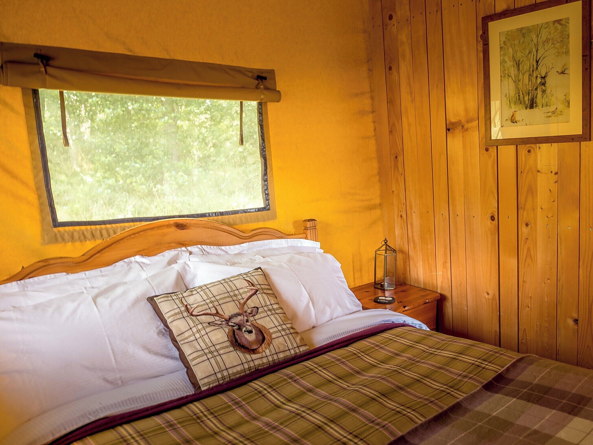 A wooden cabin room with a bed, a window, and a painting on the wall.
