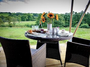 A round table with a bottle of champagne, a vase with sunflowers, and a pitcher of jam.