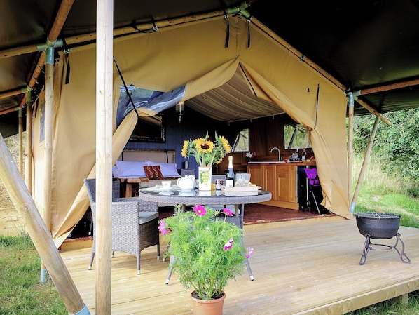 A tent with a dining area, a kitchen, and a patio with a grill and potted plants.
