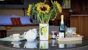 Ein runder Glastisch mit einer Sonnenblumenvase, einer Champagnerflasche, einem Teekessel, Tassen und einer Platte mit Brot.