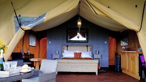 Eine Zelthütte mit einem Bett, Korbmöbeln, einem kleinen Tisch und einem Fenster.