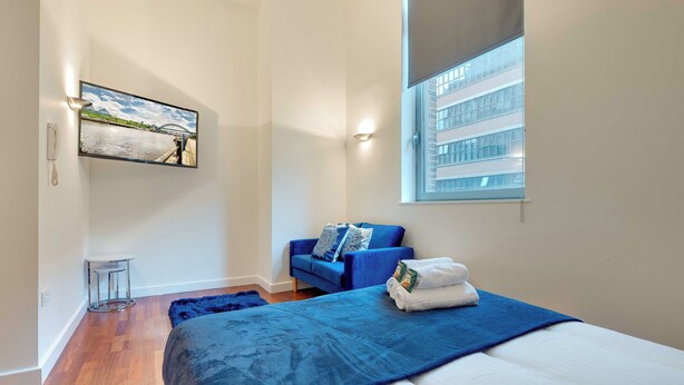 Une chambre avec un grand lit, un canapé bleu, un tableau au mur et une fenêtre avec des stores.