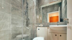 Une salle de bain moderne avec une douche à parois de verre, des toilettes blanches et un lavabo surmonté d’un miroir.