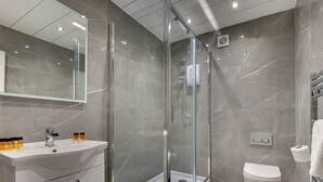 Een moderne badkamer met een douche met glazen wand, een witte wastafel met toiletartikelen en een toilet.