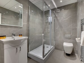 A modern bathroom with a glass-enclosed shower, a white sink with toiletries, and a toilet. - 2 bedroom accommodation in Newcastle Upon Tyne (Newcastle Upon Tyne)