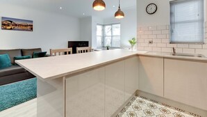 Een moderne keuken met een centraal eiland, hanglampen, een klok en een raam met zonwering.