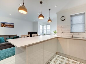 A modern kitchen with a central island, pendant lights, a clock, and a window with blinds. - 2 bedroom accommodation in Newcastle Upon Tyne (Newcastle Upon Tyne)