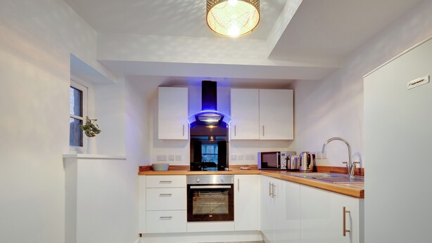 Una cocina moderna con armarios blancos, horno empotrado, microondas y hervidor.