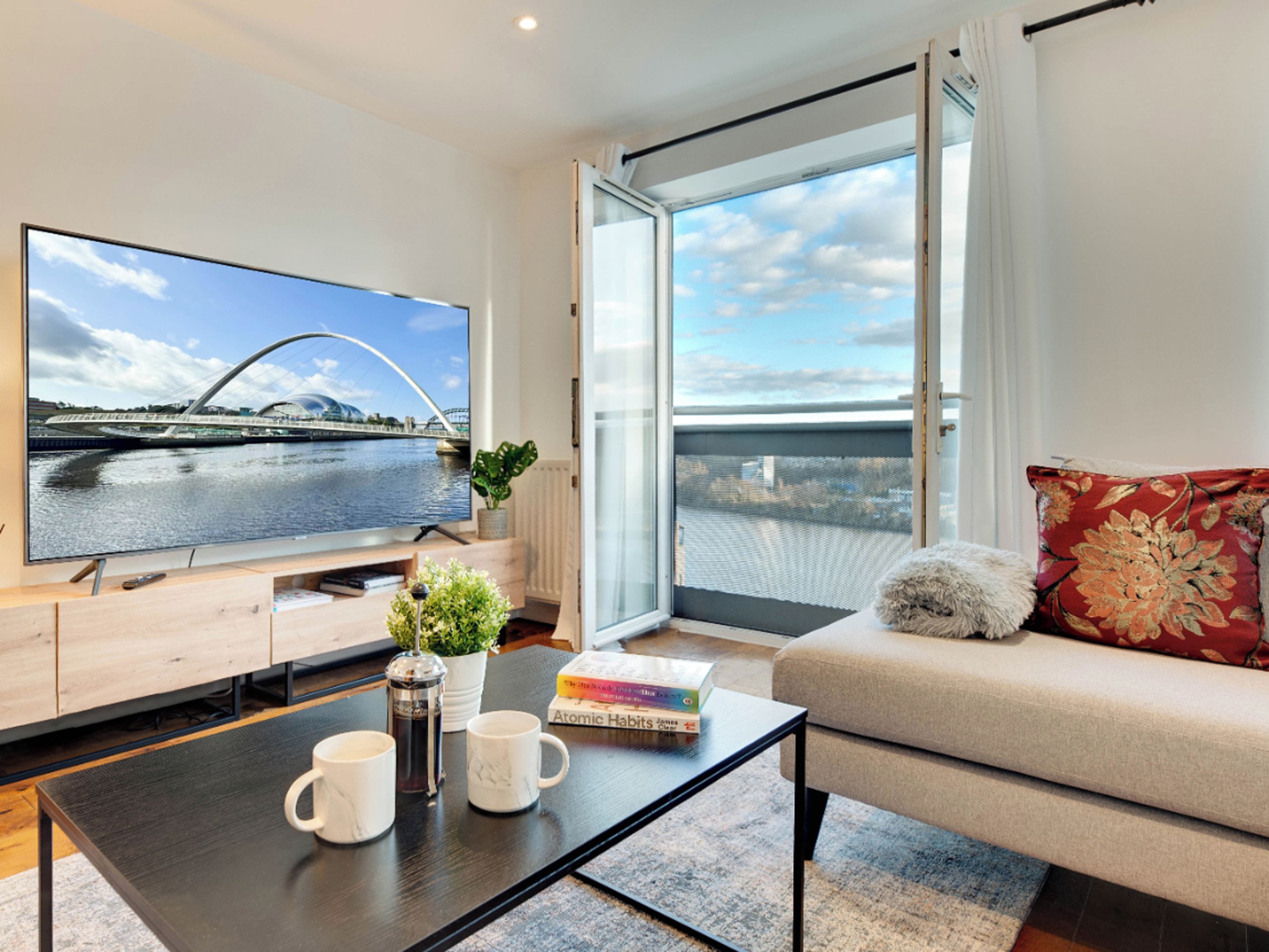 Ein modernes Wohnzimmer mit großem Flachbildfernseher, einer Couch, einem Couchtisch und Blick auf eine Brücke durch ein großes Fenster.