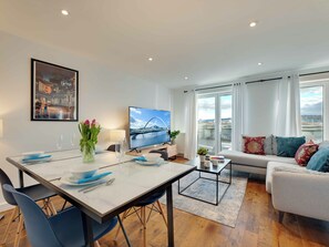 A modern living room with a dining area, a sofa, a TV, and a large window with a view. - 2 bedroom accommodation in Newcastle Upon Tyne (Newcastle Upon Tyne)