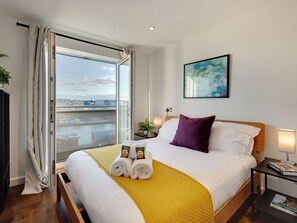 A hotel room with a bed, a view of a river, a painting on the wall, and a bedside table with a lamp. - 2 bedroom accommodation in Newcastle Upon Tyne (Newcastle Upon Tyne)