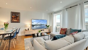 A modern living room with a sofa, dining table, chairs, a TV, and a painting on the wall. - 2 bedroom accommodation in Newcastle Upon Tyne (Newcastle Upon Tyne)