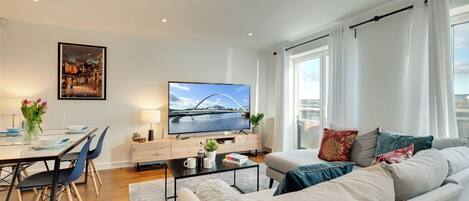 Ein modernes Wohnzimmer mit einer Couch, einem Esstisch, Stühlen, einem Fernseher und einem Bild an der Wand.