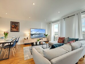 Een moderne woonkamer met een bank, eettafel, stoelen, een televisie en een schilderij aan de wand.