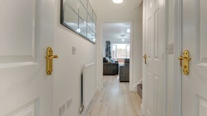 Un couloir aux murs blancs, avec un radiateur et un luminaire au plafond. Il y a deux portes dotées de poignées dorées.
