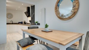 Une cuisine moderne avec des meubles blancs, une table à manger en bois et un grand miroir orné d’un cadre en forme de coquillage.
