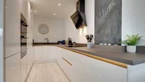 Une cuisine moderne avec des meubles blancs, un tableau noir où est écrit le mot « Bienvenue », et une plante en pot posée sur le comptoir.