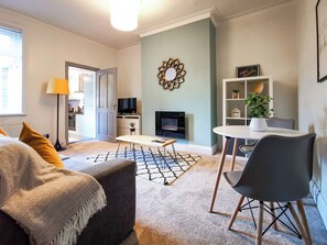 Ein modernes Wohnzimmer mit einer Couch, einem Couchtisch, einem Fernseher, einem Kamin und einem Bücherregal.