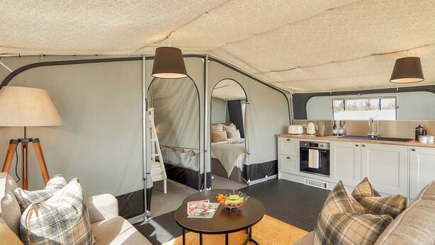 A compact, well-lit tent with a kitchenette, a bed with a canopy, and a seating area with a table. - 2 bedroom accommodation in Rhayader and the Elan Valley (Rhayader and the Elan Valley)