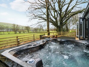 A hot tub area with a wooden deck, a large tree, and a view of the countryside.