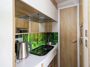Una cocina compacta con estufa moderna, hervidor y lavamanos.